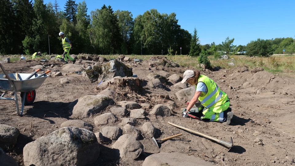 Utgrävningsplats med två personer som arbetar framför en skog.