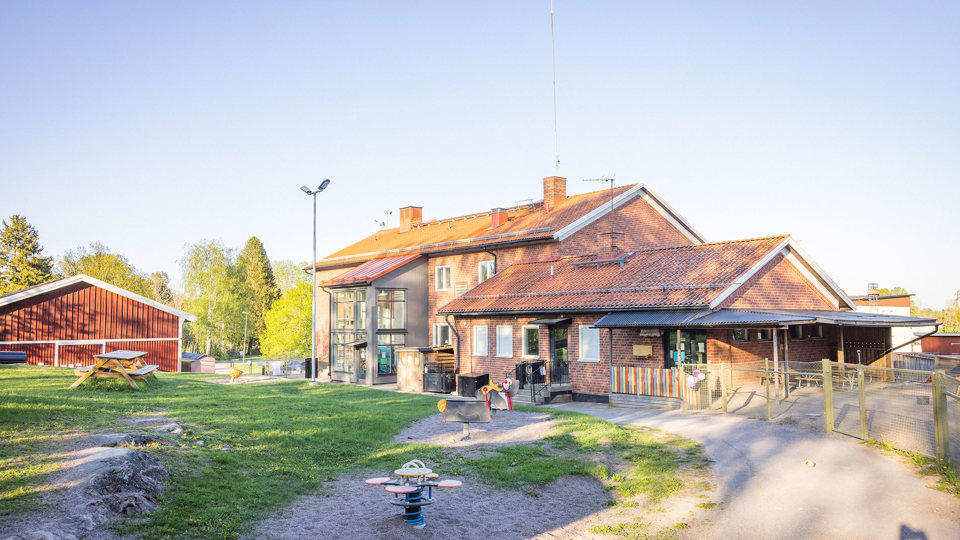 Förskola i brunt tegel med gård och lekutrustning i förgrunden.
