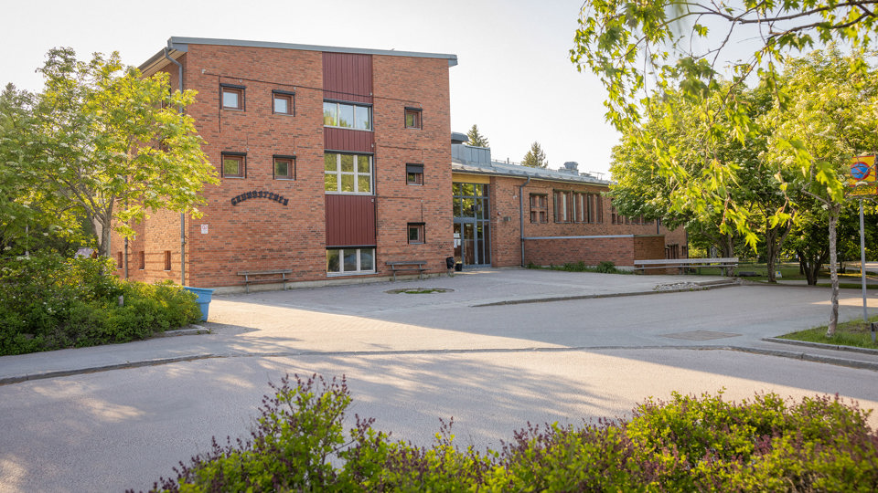 Skolbyggnad i brunt tegel med omgivande gröna träd och buskar