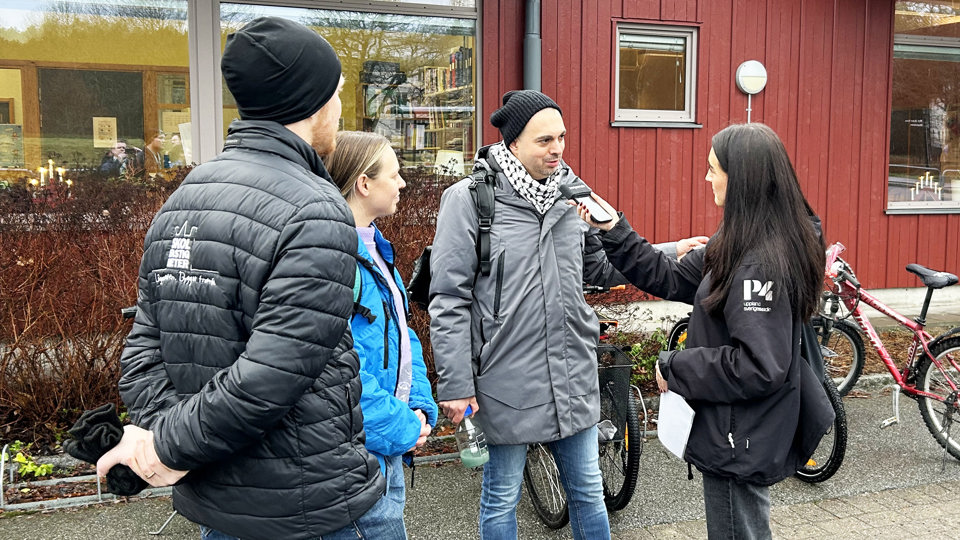 En man blir intervjuad av en journalist och två personer står bredvid och lyssnar.
