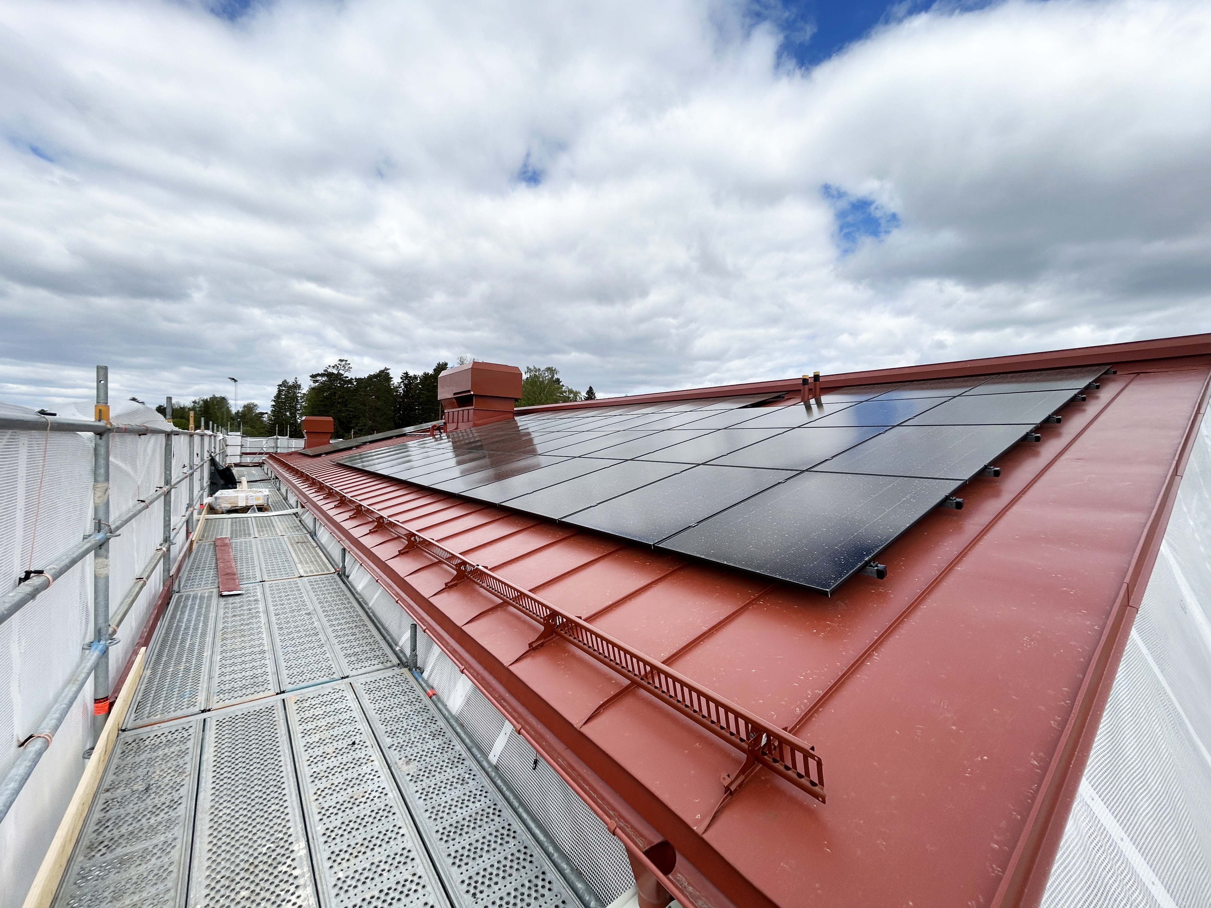Rött plåttak med solcellspaneler på en ny förskola som håller att byggas.