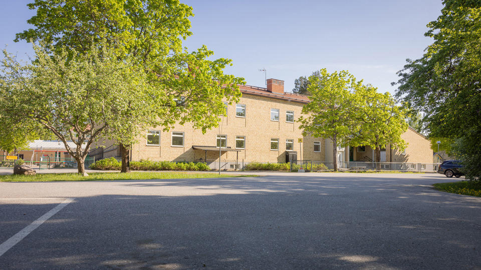 Skolbyggnad i gult tegel med asfaltyta i förgrunden