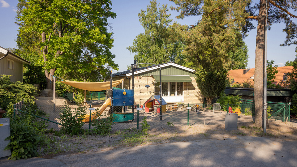 Gul tegelförskola med gård, klätterställning och lekutrustning i förgrunden.