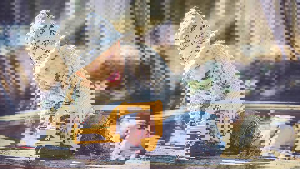 En liten förskolepojke leker med en gul grävmaskin i en sandlåda