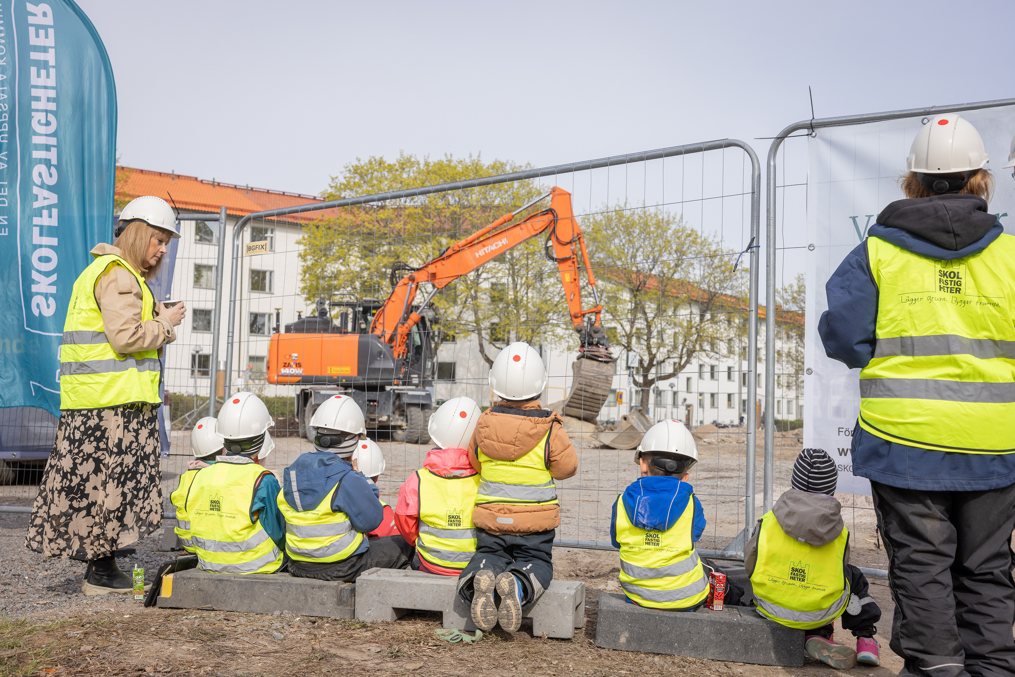 Förskolebarn fikar och tittar på grävmaskin efter ett spadtag i bygget av ny förskola.
