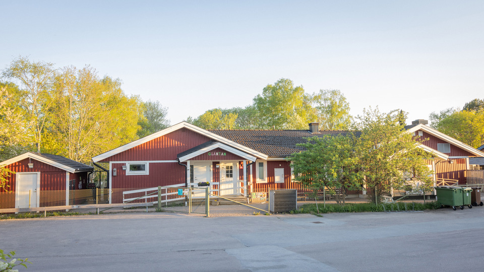 Röd förskola i trä med gröna träd och buskar i bakgrunden.
