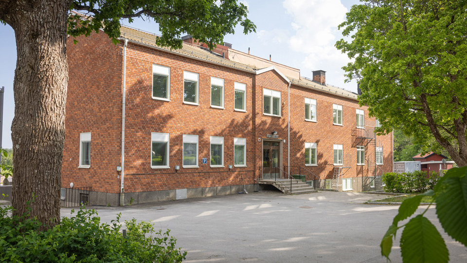 Brun tegelbyggnad med omgivande gröna träd och buskar