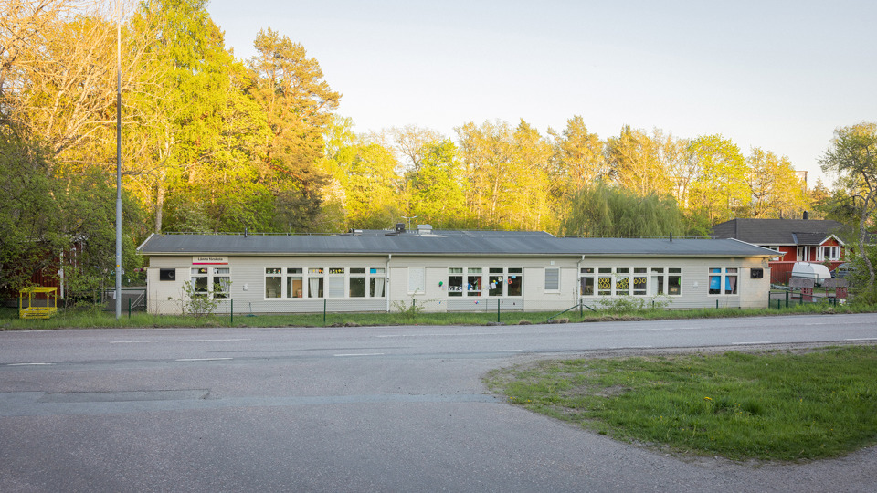 Grå förskolebyggnad med en bilväg i förgrunden