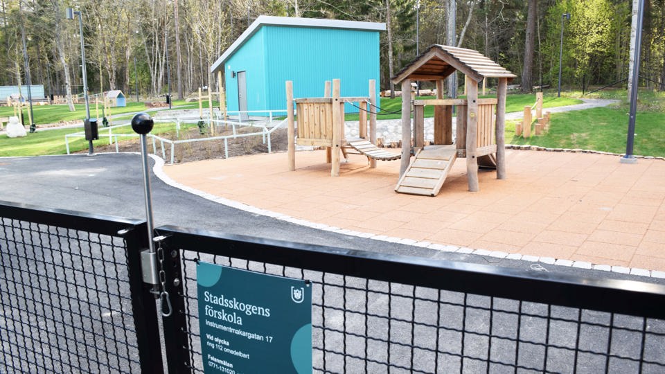 Förskolegård med lekutrustning i trä och skog i bakgrunden.