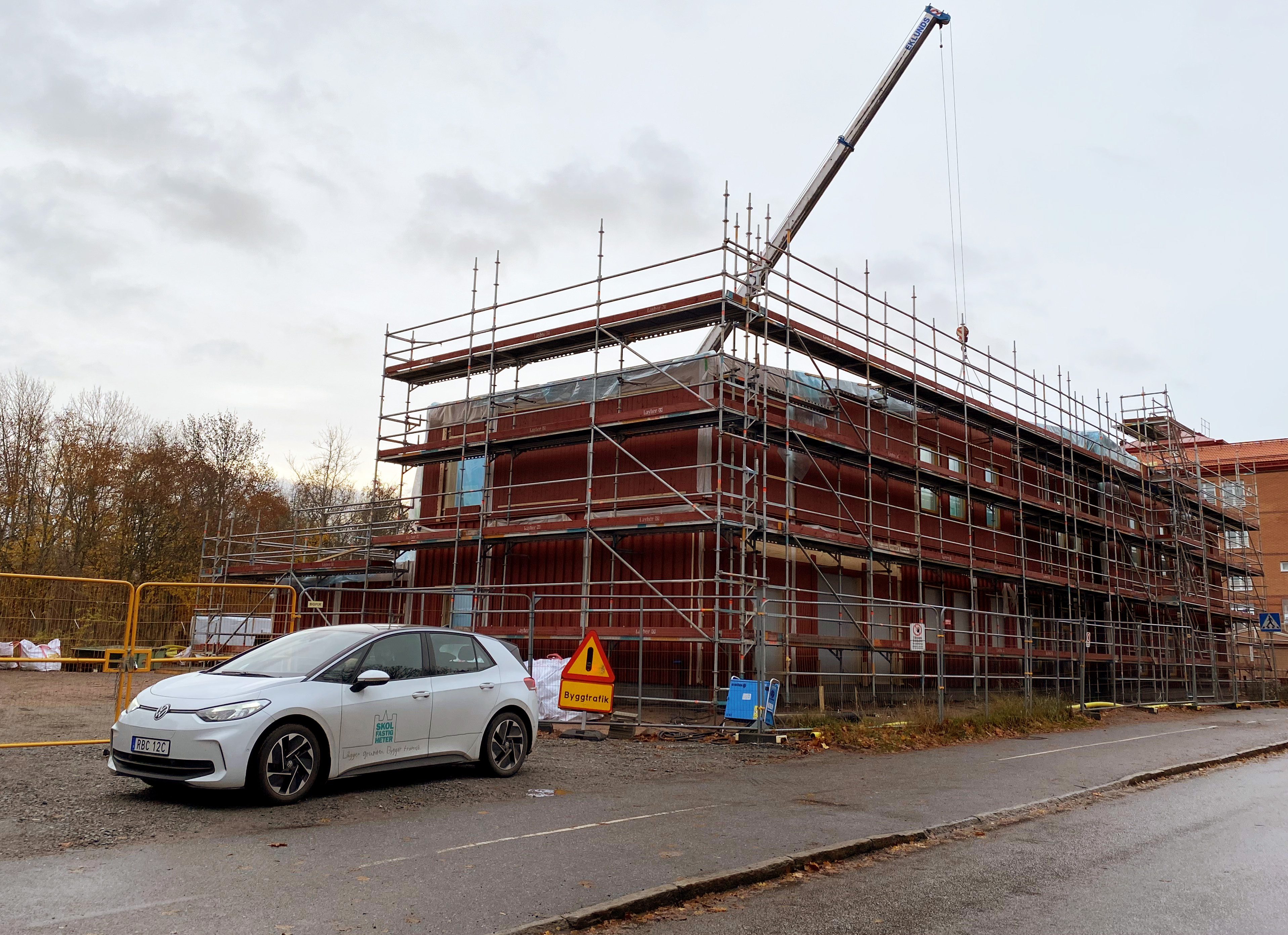 Byggplats där en ny, röd förskola i trä håller på att byggas. 