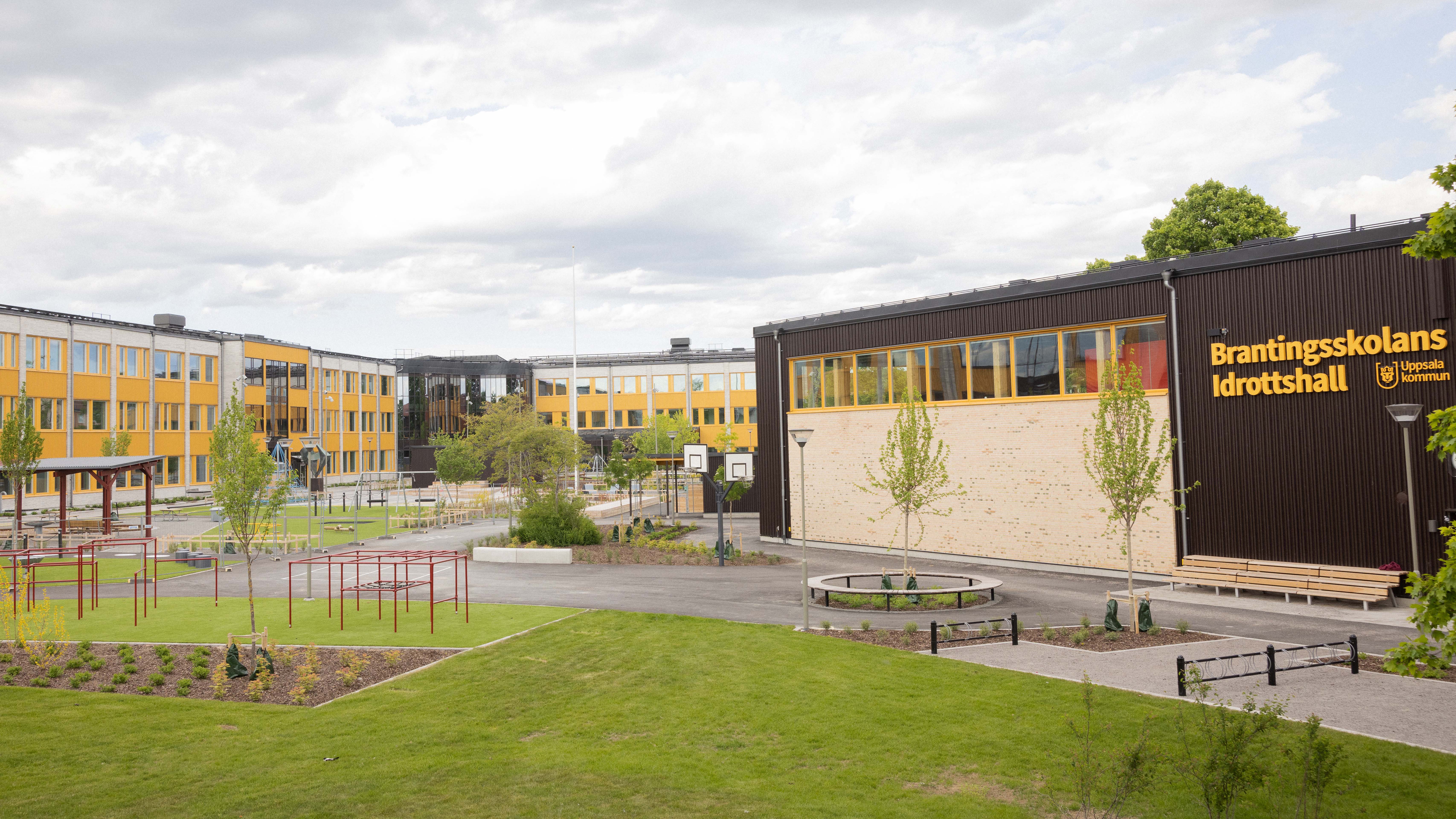 Skola med grön skolgård och lekutrustning i förgrunden.