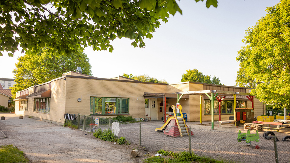 Förskola i gult tegel med skolgård, grusplan och lekutrustning