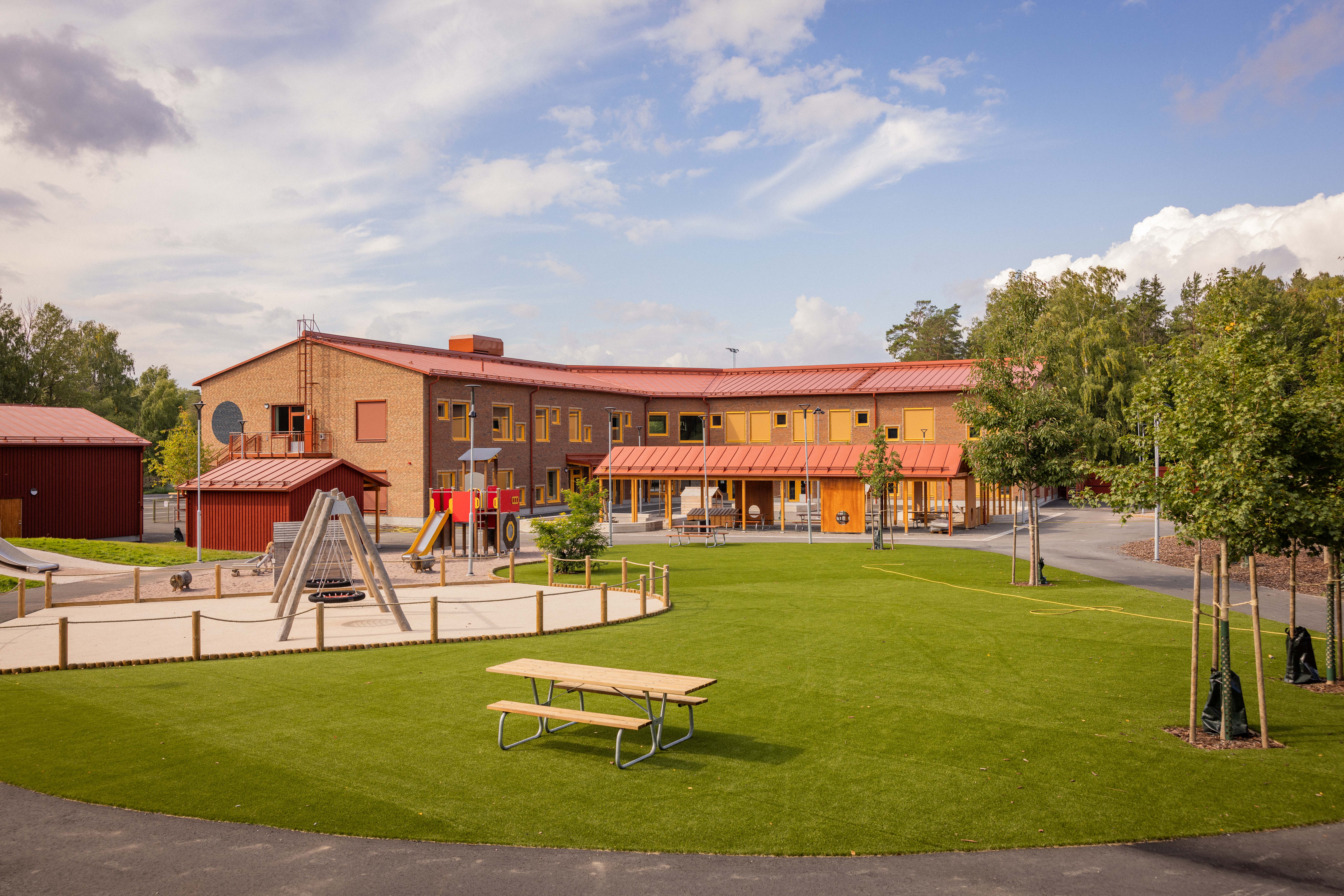 Nybyggd förskola med grön gård och lekutrustning i förgrunden 