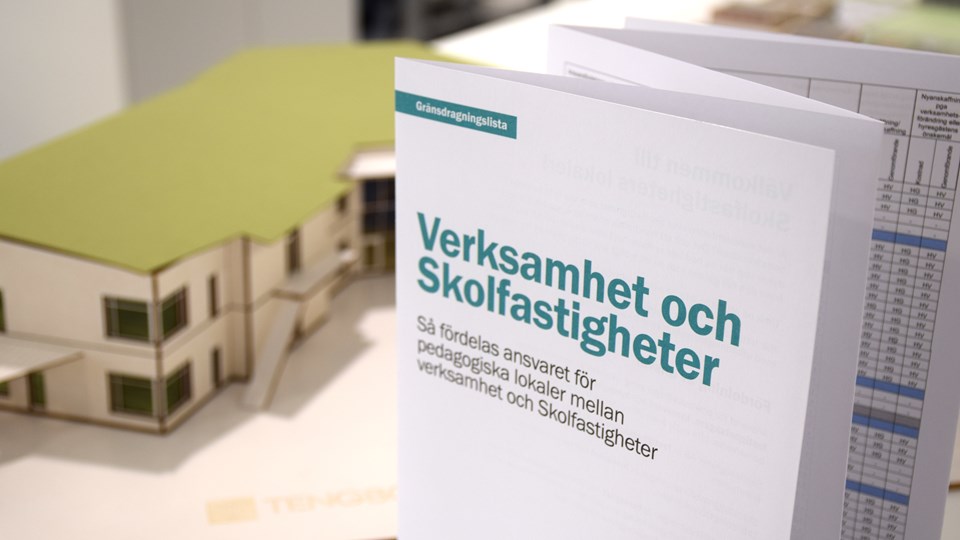 Folder med fastighetsinformation som står på ett bord framför en modell av en förskola.