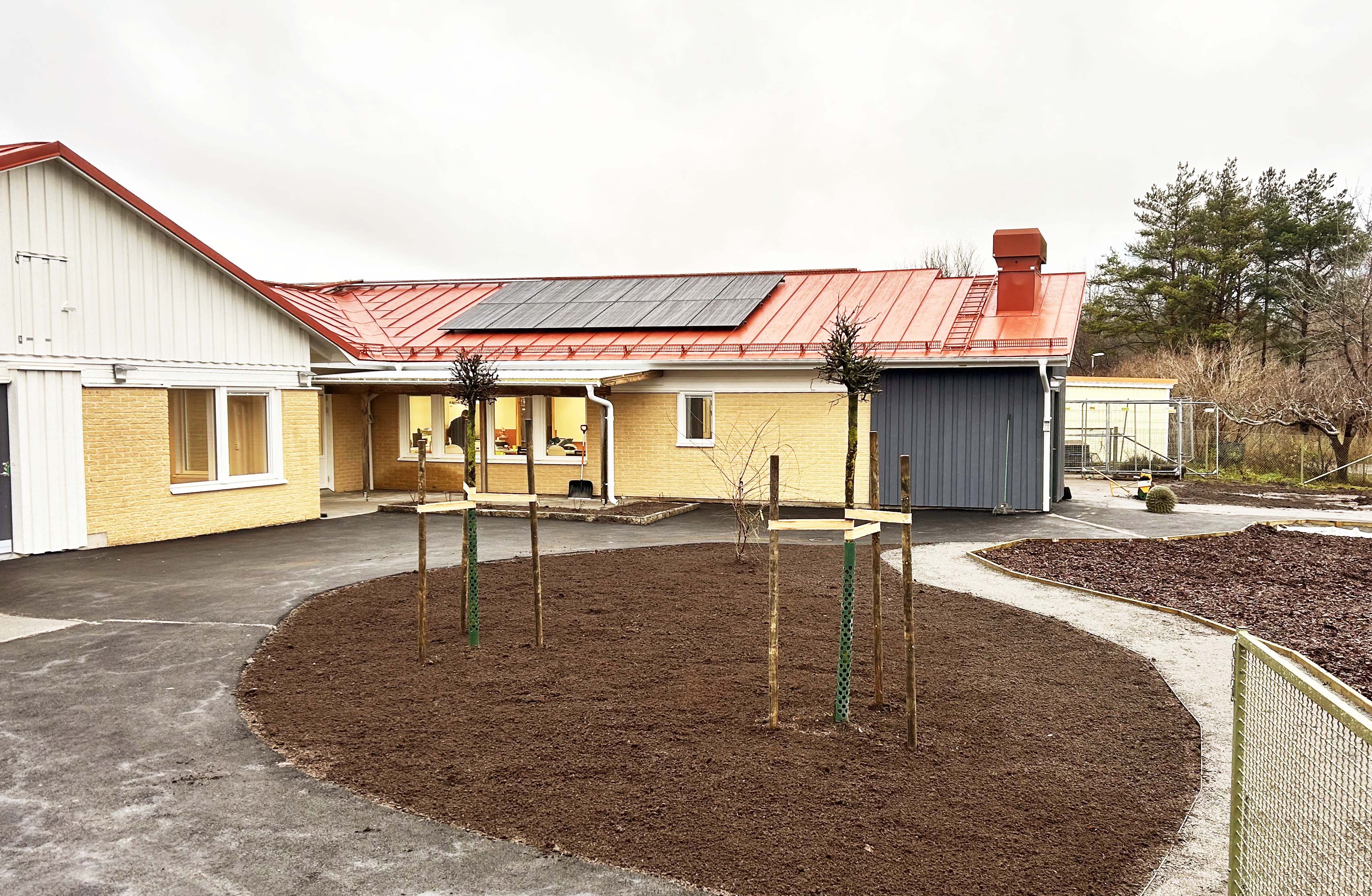 Nyrenoverad förskolebyggnad i tegel med nyplanterade träd i förgrunden.