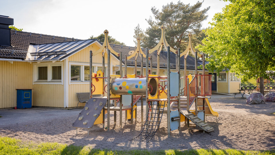 Gul klätterställning på grusyta framför en förskola.