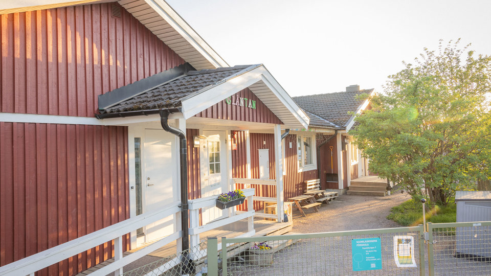 Röd förskola med grind in till förskolegård i förgrunden.