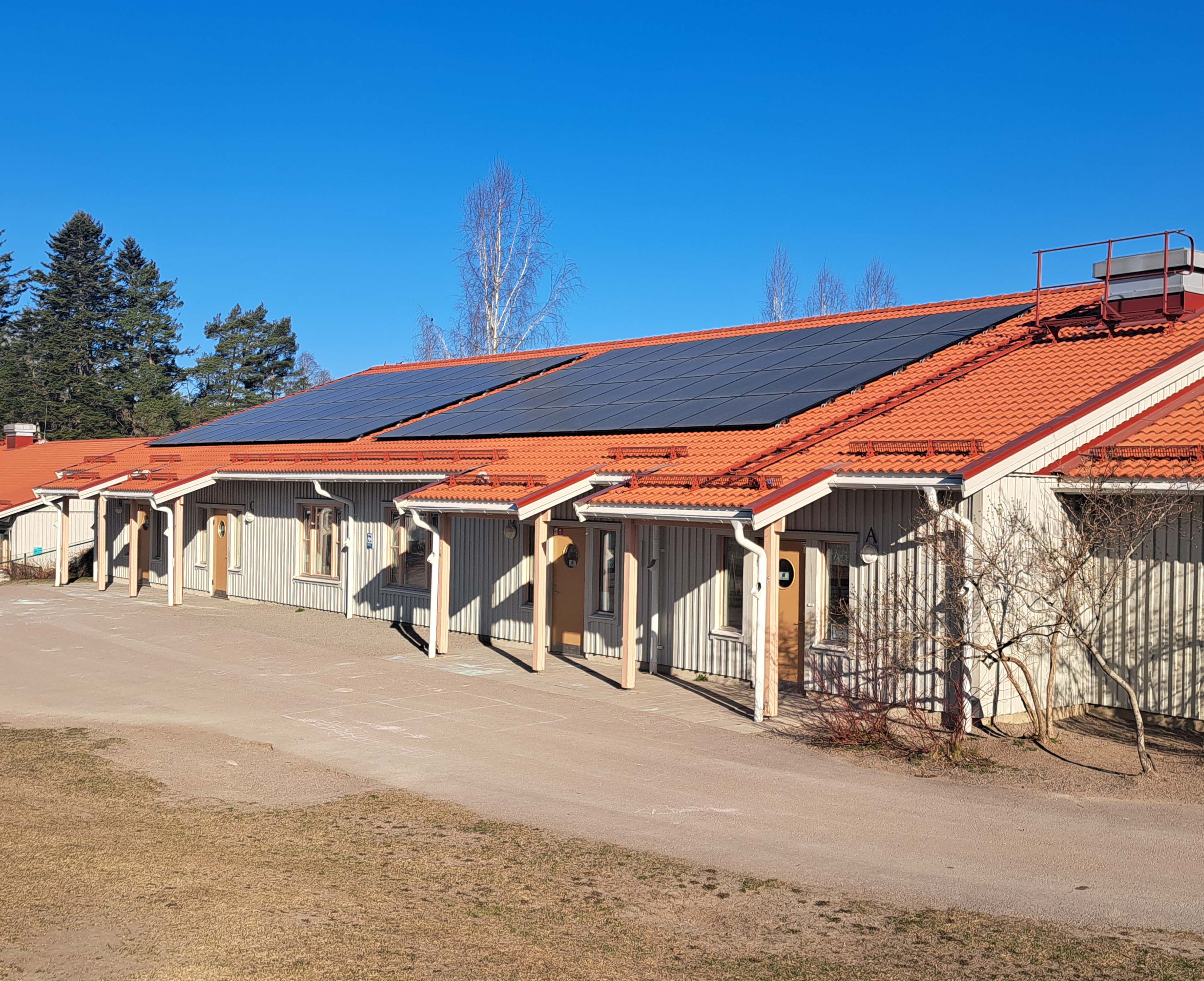 Nylagt tak med solcellsanläggning på skola med rött tegeltak och träfasad