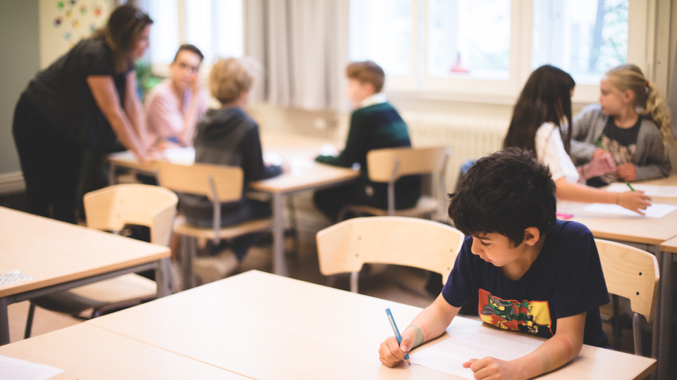 Skolbarn som arbetar vid bänkar i ett klassrum.