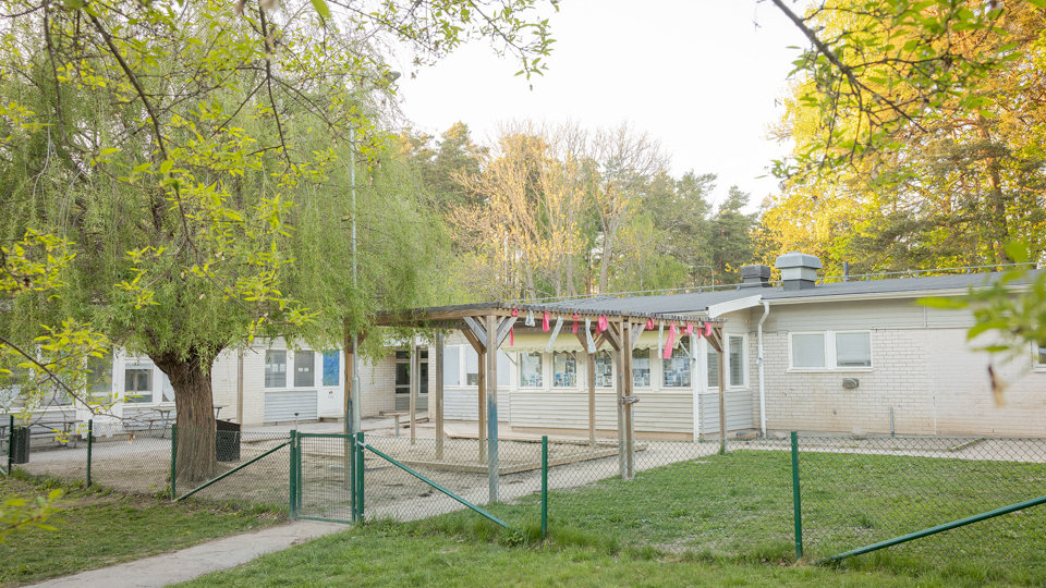 Förskolebyggnad i grått tegel med utemiljö i förgrunden