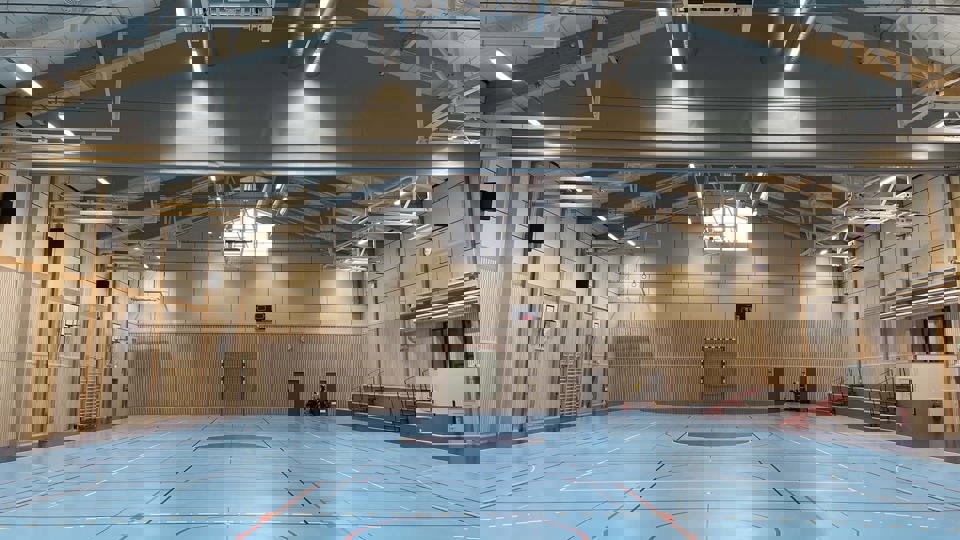 Idrottshall med blått golv, läktare och basketkorgar.