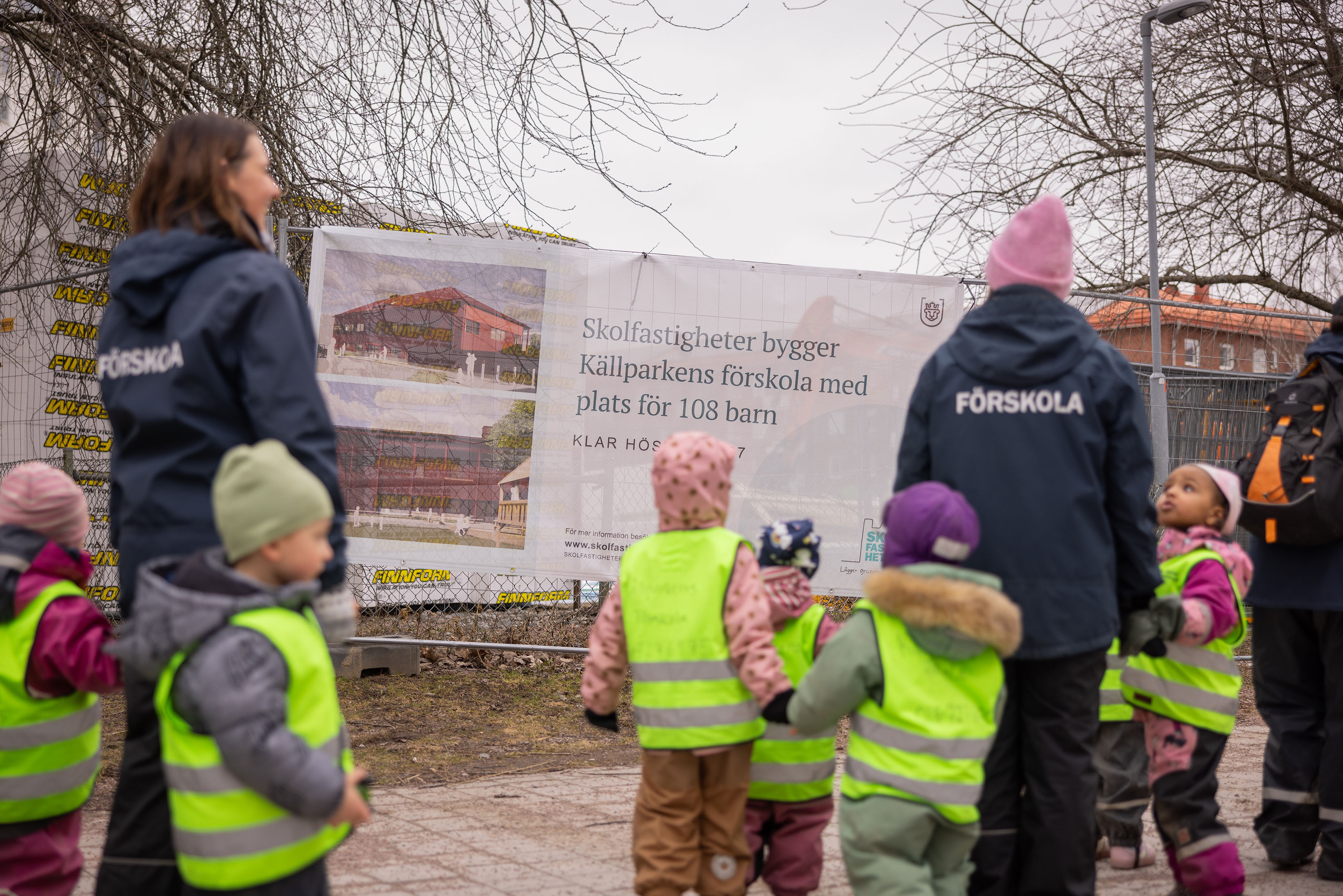 En grupp förskolelärare och barn tittar på en vepa med bild på en förskola som ska byggas.