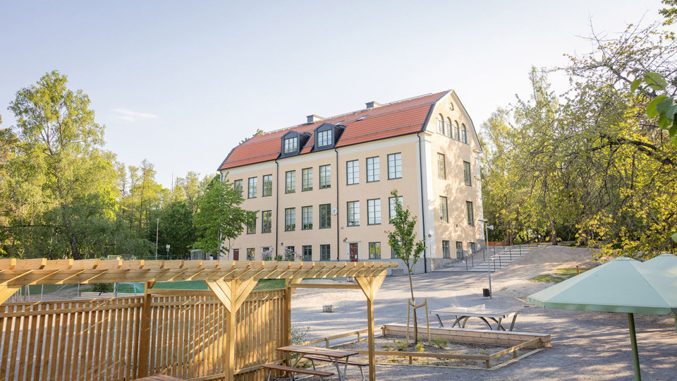 Gul skolbyggnad med skolgård och bänkar i förgrunden